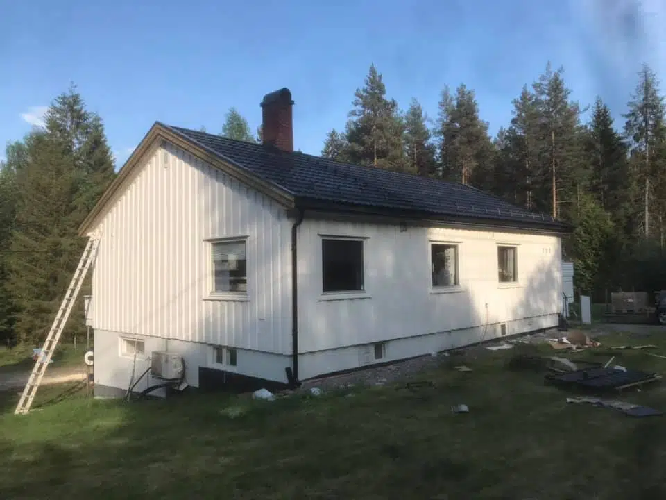 Hvitt hus med sort tak og en hage